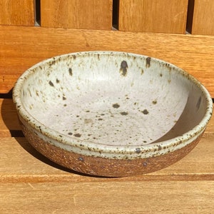 May include: A white ceramic bowl with brown speckles and a brown rim. The bowl is sitting on a wooden surface.