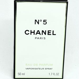 May include: A rectangular Chanel No. 5 Eau de Parfum box with a white front panel and black border. The text reads N&deg;5, CHANEL, PARIS, EAU DE PARFUM, VAPORISATEUR SPRAY, 50 ml, and 1.7 FL.OZ. The packaging features clean, minimalist typography.