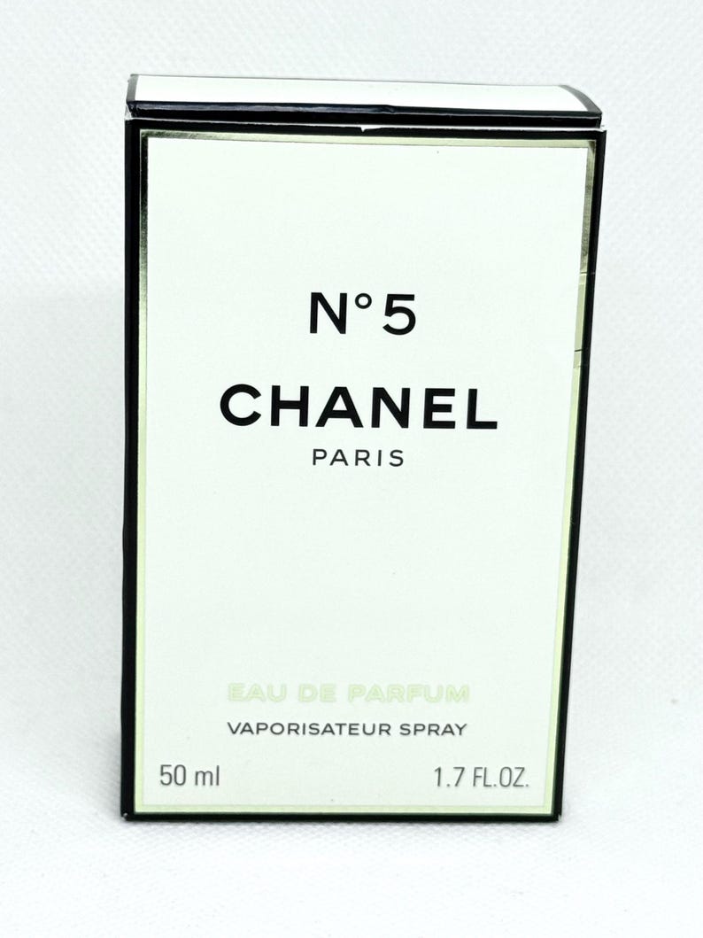 May include: A rectangular Chanel No. 5 Eau de Parfum box with a white front panel and black border. The text reads N&deg;5, CHANEL, PARIS, EAU DE PARFUM, VAPORISATEUR SPRAY, 50 ml, and 1.7 FL.OZ. The packaging features clean, minimalist typography.