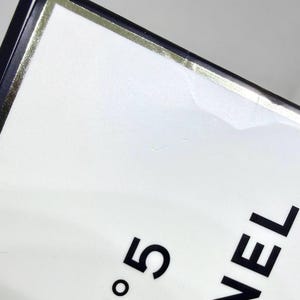 May include: A white rectangular box with a black border and a thin gold metallic trim. The text N&deg;5 is printed in black, with the letters ANEL and RIS partially visible below it, indicating the branding on this fragrance packaging.