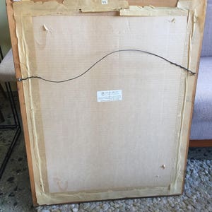 May include: The back of a framed picture with a brown wooden frame and a cardboard backing. The frame has a label that says "44" and a sticker that says "Certificate of Guarantee".