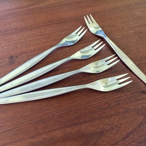 May include: Five silver forks with a polished finish. The forks are arranged in a fan shape on a wooden surface.