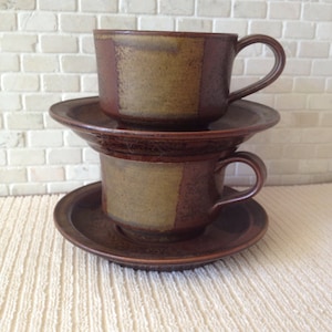 May include: Two brown and tan ceramic coffee cups with matching saucers. The cups have a geometric pattern.