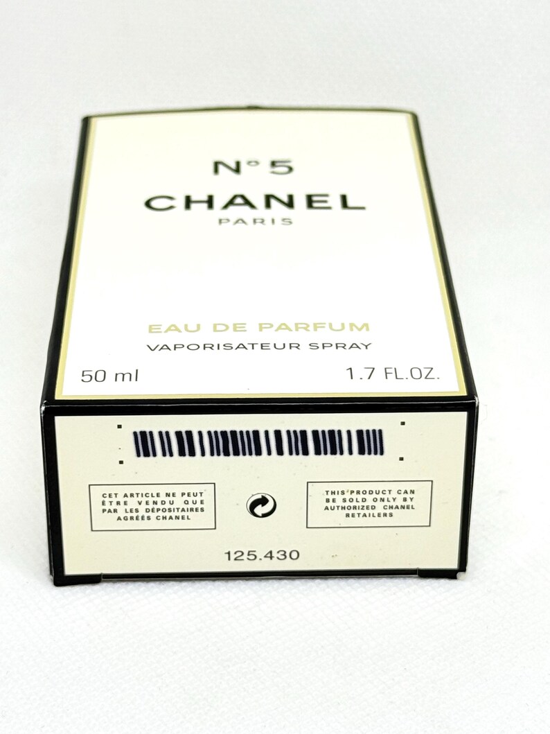 May include: A rectangular Chanel No. 5 Eau de Parfum box in white with black trim. The front displays the text N&deg; 5 CHANEL PARIS, EAU DE PARFUM, VAPORISATEUR SPRAY, 50 ml, and 1.7 FL.OZ. The bottom edge features a barcode and retail text.
