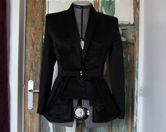 May include: A black satin blazer with a peplum hem and a single button closure. The blazer is on a mannequin in front of a wooden door.
