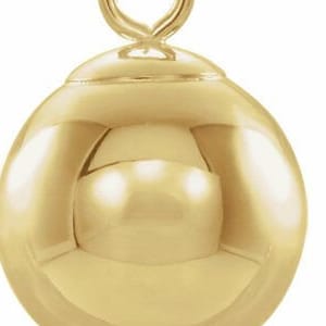 May include: A gold-toned ball charm with a loop at the top. The ball is smooth and shiny.