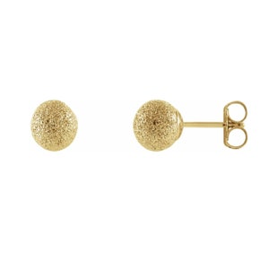 May include: A pair of gold-colored stud earrings. Each earring features a textured, spherical design. One earring is shown with the post and butterfly backing visible. The earrings are set against a white background.