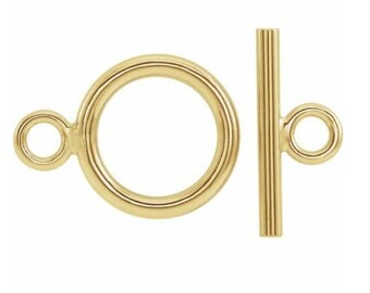 May include: Gold-toned metal toggle clasp with a round ring and a straight bar. The ring has a smaller ring attached to it.