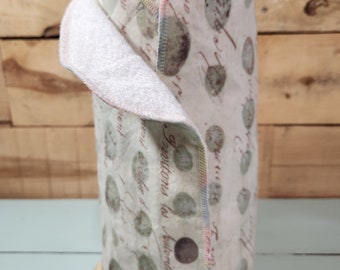 May include: A roll of reusable paper towels with a white background and a green and brown floral pattern. The towels are sewn with a light blue, pink, and yellow trim. The roll is on a wooden stand.