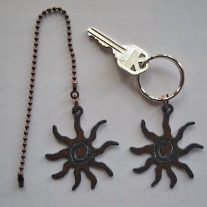 May include: Two copper chain pull pendants with a sun design. The pendants are attached to a key ring with a silver key.