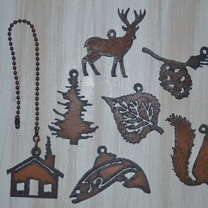 May include: A set of nine rustic metal ornaments featuring a deer, pine tree, leaf, pine cone, squirrel, cabin, and fish. The ornaments are all brown and have a distressed look. They are perfect for adding a touch of nature to your home decor.