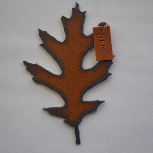 May include: A brown ceramic leaf with a gray outline. The leaf has a tag attached to it that says "NAME".