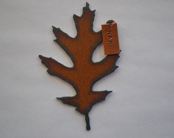 May include: A brown ceramic leaf with a gray outline. The leaf has a tag attached to it that says "NAME".