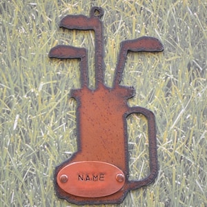 May include: A rusty brown metal golf bag silhouette with three golf clubs. The golf bag has a handle and an oval-shaped tag with the word 
