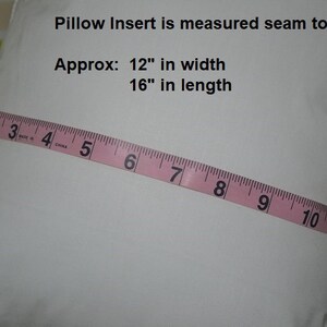 May include: A white pillow insert with a pink measuring tape across it. The tape reads "2 3 4 5 6 7 8 9 10 11 12 13". Text on the pillow reads "Pillow Insert is measured seam to seam Approx: 12" in width 16" in length"