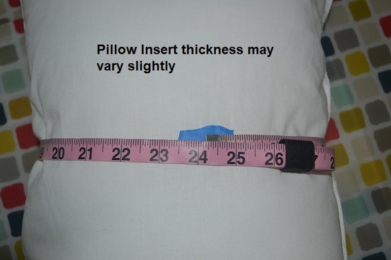 May include: A white pillow with a pink measuring tape wrapped around it. The tape reads "20, 21, 22, 23, 24, 25, 26". The text "Pillow Insert thickness may vary slightly" is printed on the pillow.