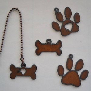 May include: Four metal dog-themed fan pulls with a heart cut-out. Two are bone-shaped, one is a paw print, and one is a paw print with a heart cut-out. The fan pulls are attached to a copper chain.