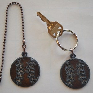 May include: Two copper-toned baseball-shaped keychains with a chain and a key ring. The keychains have a cut-out design of baseball stitching.