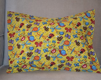 May include: Yellow pillowcase with a colorful pattern of cartoon bugs, including bees, butterflies, snails, and ladybugs. The word "Bugs" is written in a playful font. The pillow is resting on a gray chair.
