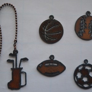 May include: Six metal fan pull chains with different sports themes. The chains are copper colored and have a brown patina. The sports themes include golf, basketball, baseball, football, and soccer.