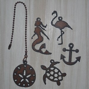 May include: A set of six metal fan pull charms featuring a mermaid, a flamingo, an anchor, a sea turtle, and a sand dollar. The charms are all in a rusty brown color.