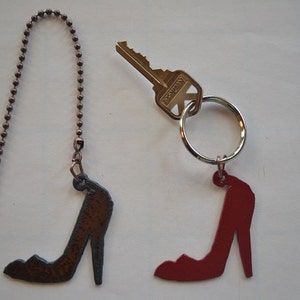 May include: Two metal shoe-shaped charms, one red and one brown, attached to keychains. The red charm is attached to a silver key ring with a key. The brown charm is attached to a copper chain.