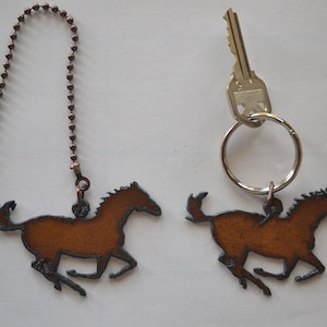 May include: Two brown metal horse silhouettes, one attached to a chain and the other to a key ring. The horse silhouettes are a rustic brown color and have a distressed finish.