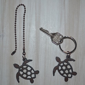 May include: Two metal turtle keychains, one attached to a silver key and key ring, the other attached to a brown chain. Both turtles have a cutout design and are a dark brown color.