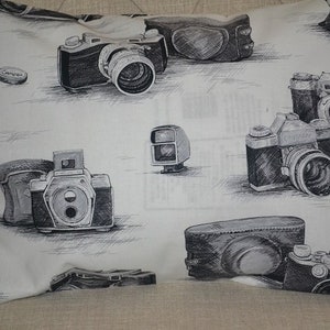 May include: A white pillowcase with a black and white pattern of vintage cameras. The pillowcase features a variety of camera styles, including a 35mm camera, a rangefinder camera, and a box camera.