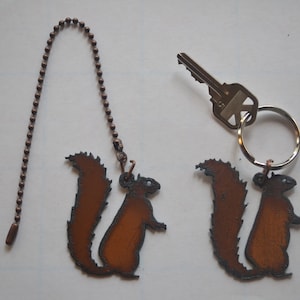 May include: Two metal squirrel keychains, one attached to a copper chain and the other to a silver key ring. The squirrels are brown with a black outline.