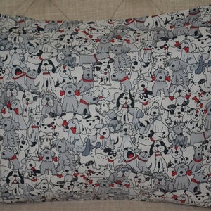 May include: Rectangular pillow with a repeating pattern of cartoon dogs in various poses. The dogs are primarily gray and white, with red accents like bow ties and bones. The pillowcase is made of a light-colored fabric.