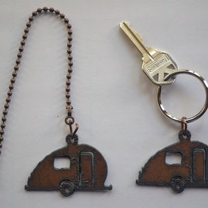 May include: Two keychains with a brown metal camper trailer design. One keychain has a copper chain and the other has a silver key ring with a silver key.