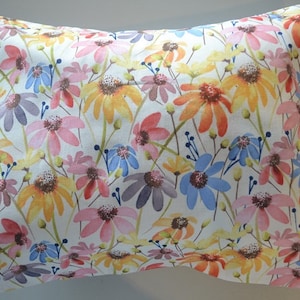 May include: A white pillowcase with a floral pattern featuring pink, yellow, blue, and purple flowers. The flowers are painted in a watercolor style and are scattered across the fabric.