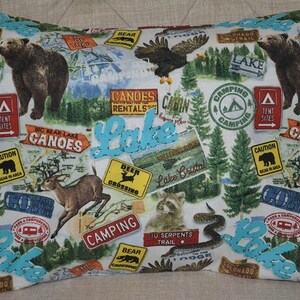 May include: A white pillowcase with a colorful pattern of camping and lake-themed imagery. The pattern includes bears, deer, trees, and signs with text like "Lake", "Camping", "Canoes", and "Colorado Trail".
