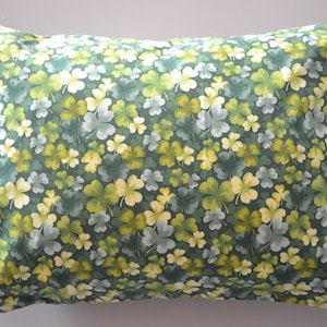 May include: A rectangular pillow with a green background covered in a pattern of shamrocks in shades of green, yellow, and white. The pillow has a soft, inviting appearance, perfect for home decor.