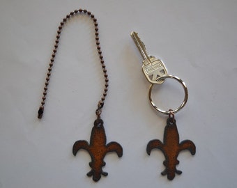 May include: Two rusty brown fleur-de-lis charms, one attached to a copper chain and the other to a silver key ring.