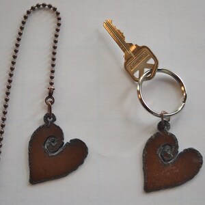 May include: Two metal heart-shaped charms with a swirl design, one attached to a key ring with a key and the other attached to a chain.