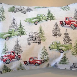 May include: A white pillowcase with a repeating pattern of red and green vintage pickup trucks carrying Christmas trees. The trucks are on a white background with a subtle green and brown pattern.