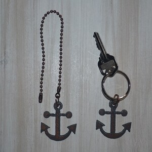 May include: Two anchor-shaped keychains, one with a silver chain and the other with a silver key ring. Both anchors are a dark brown color.