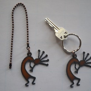 May include: Two brown metal keychains with a stylized Native American dancer design. One keychain is attached to a copper chain and the other is attached to a silver key ring.