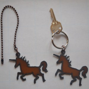 May include: Two brown metal unicorn charms. One charm is attached to a silver key ring with a key. The other charm is attached to a brown metal chain.