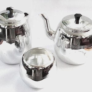 May include: A silver tea set with a teapot, a creamer, and a sugar bowl. The teapot has a black handle and lid. The creamer and sugar bowl are round. The set is on a white background.