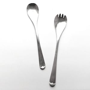 Könnte beinhalten: Zwei silberne Servierutensilien: ein Löffel und eine Gabel. Der Löffel hat eine abgerundete Schüssel und einen langen Griff. Die Gabel hat drei Zinken. Beide Utensilien haben ein dekoratives, gewelltes Design am Ende des Griffs.
