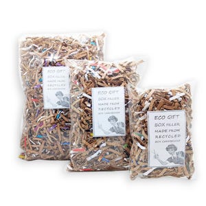 May include: Three clear plastic bags filled with brown shredded paper. Each bag has a white label that reads "ECO GIFT BOX FILLER MADE FROM RECYCLED BOX CARDBOARD". The bags are different sizes.