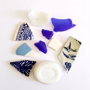 May include: An assortment of sea glass and ceramic shards in shades of blue, white, and cream. The pieces include fragments of patterned pottery and smooth, rounded sea glass, creating a collection of coastal-inspired elements.
