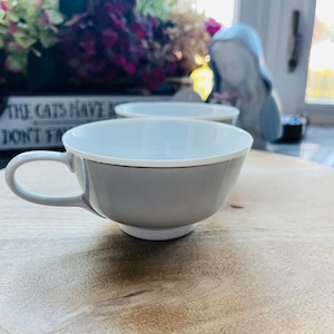 May include: Two gray ceramic teacups with a gold rim on a wooden surface. The teacups are empty and ready for a warm beverage.