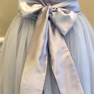 May include: A light gray tulle skirt with a matching satin sash tied in a bow at the waist.