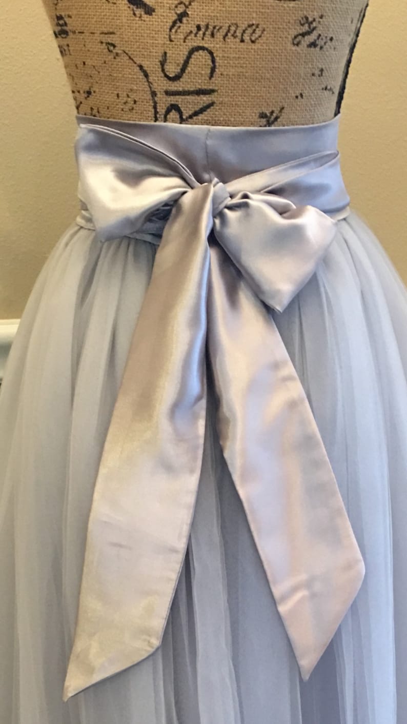 May include: A light gray tulle skirt with a matching satin sash tied in a bow at the waist.