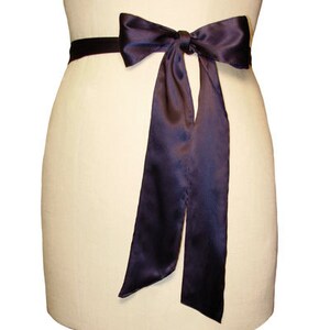 May include: A dark purple satin ribbon tied in a bow around a waist. The ribbon is long and flowing, with the ends trailing down the sides.