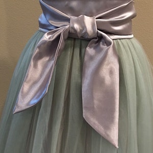 May include: A light green tulle skirt with a wide silver satin sash tied in a bow at the front.